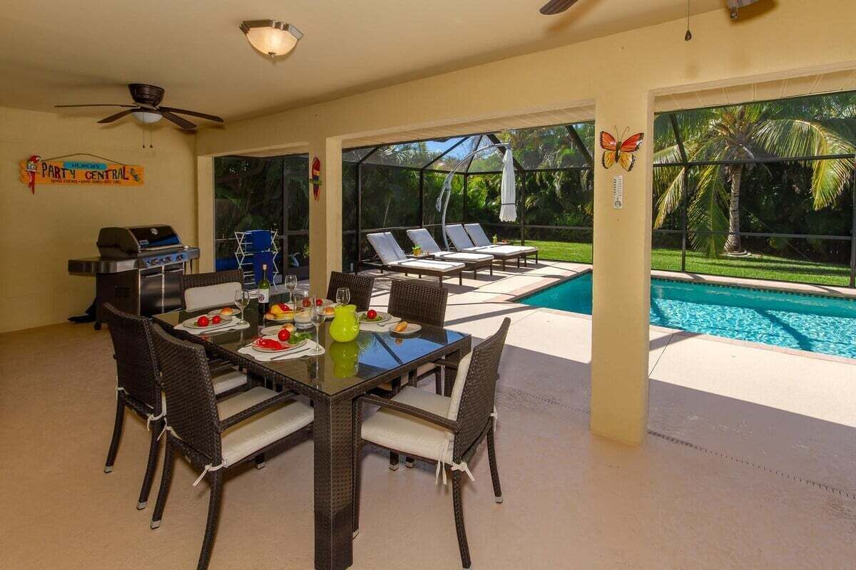 Un espace repas avec vue sur la piscine, des sièges d’extérieur et un barbecue.