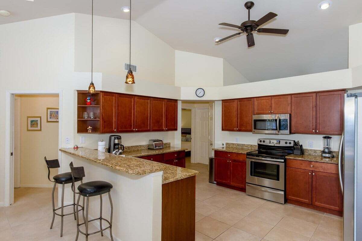 Una cocina con armarios de madera, una isla central con taburetes de bar, un ventilador de techo y un microondas.