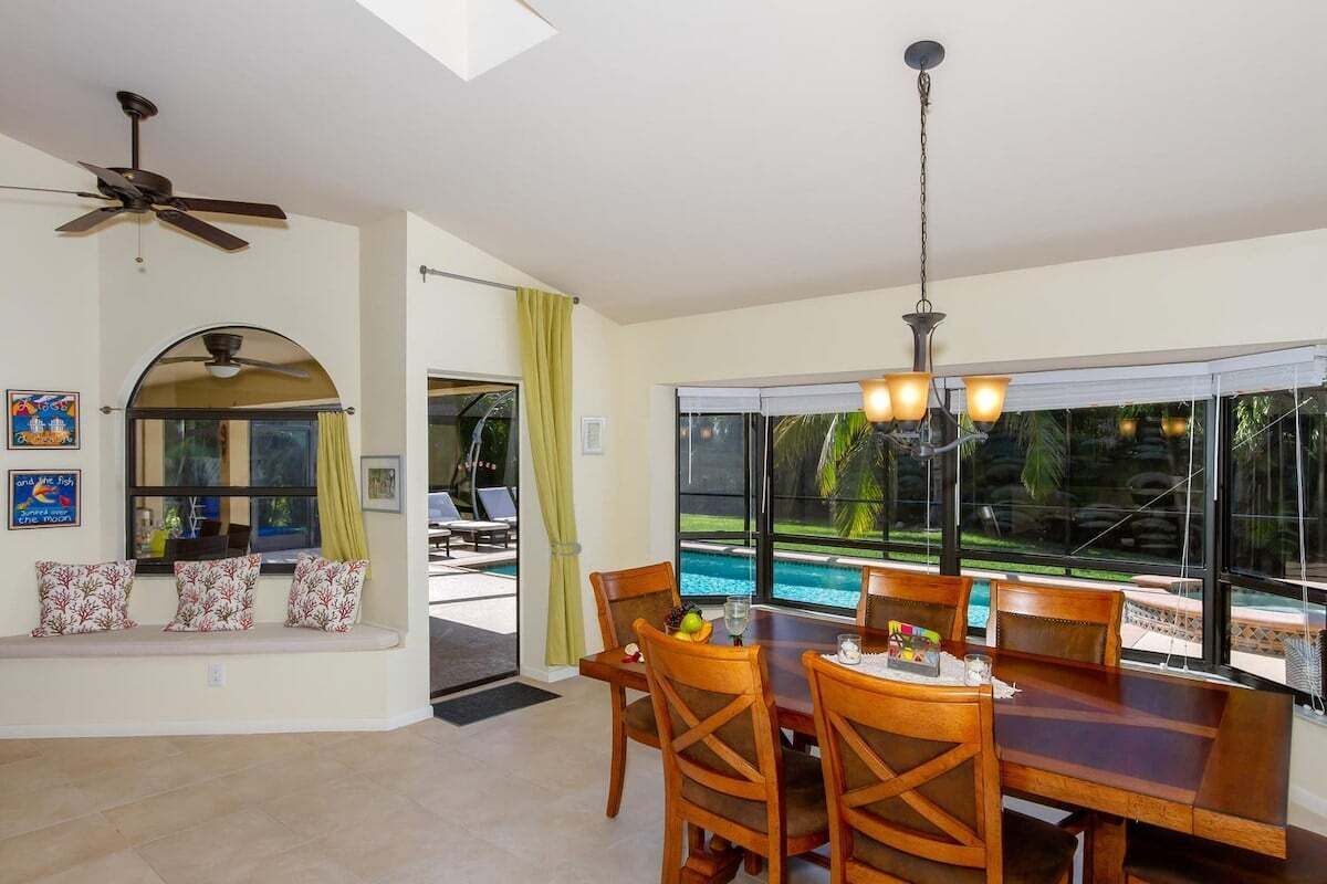 A dining area with a table and chairs, a ceiling fan, and a view of a swimming pool.
