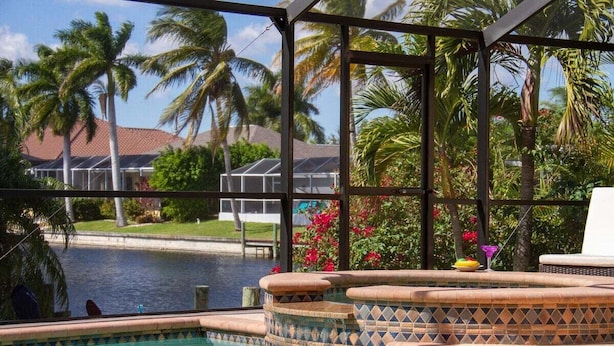 A pool area with a view of palm trees and a building in the background. - Ellen`s House-pool and Jacuzzi, Gulf access (Cape Coral)