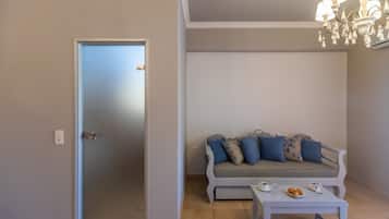 Una habitación con la puerta cerrada, un sofá gris con cojines azules, una mesa blanca con un plato de croissants y una araña.