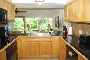 A kitchen with wooden cabinets, a stainless steel sink, a microwave, a coffee maker, and a view of greenery outside.