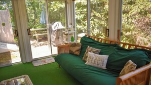 Une pièce avec un canapé vert, une tête de lit en bois et une porte en verre donnant sur un espace extérieur équipé d’une table de pique-nique et d’un parasol.