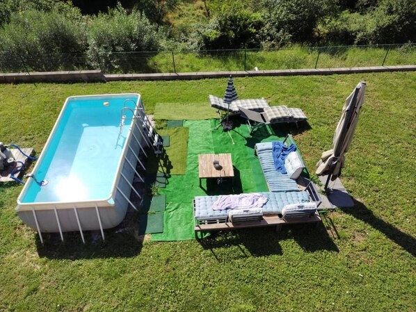 Una piscina exterior con escalera, rodeada de colchonetas verdes y sillones de descanso.