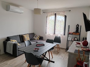 A modern living room with a sofa, dining table, chairs, and a kitchen area with a stove and cabinets. - Les Chataigniers (Saint-Sebastien-d'Aigrefeuille)
