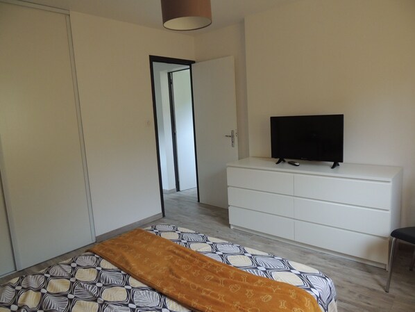 Un dormitorio con cama, televisor en una cómoda y puerta que da a otra habitación.