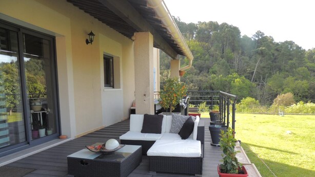 A modern outdoor seating area with a sofa and a coffee table, surrounded by potted plants and a view of a forested area. - Les Chataigniers (Saint-Sebastien-d'Aigrefeuille)
