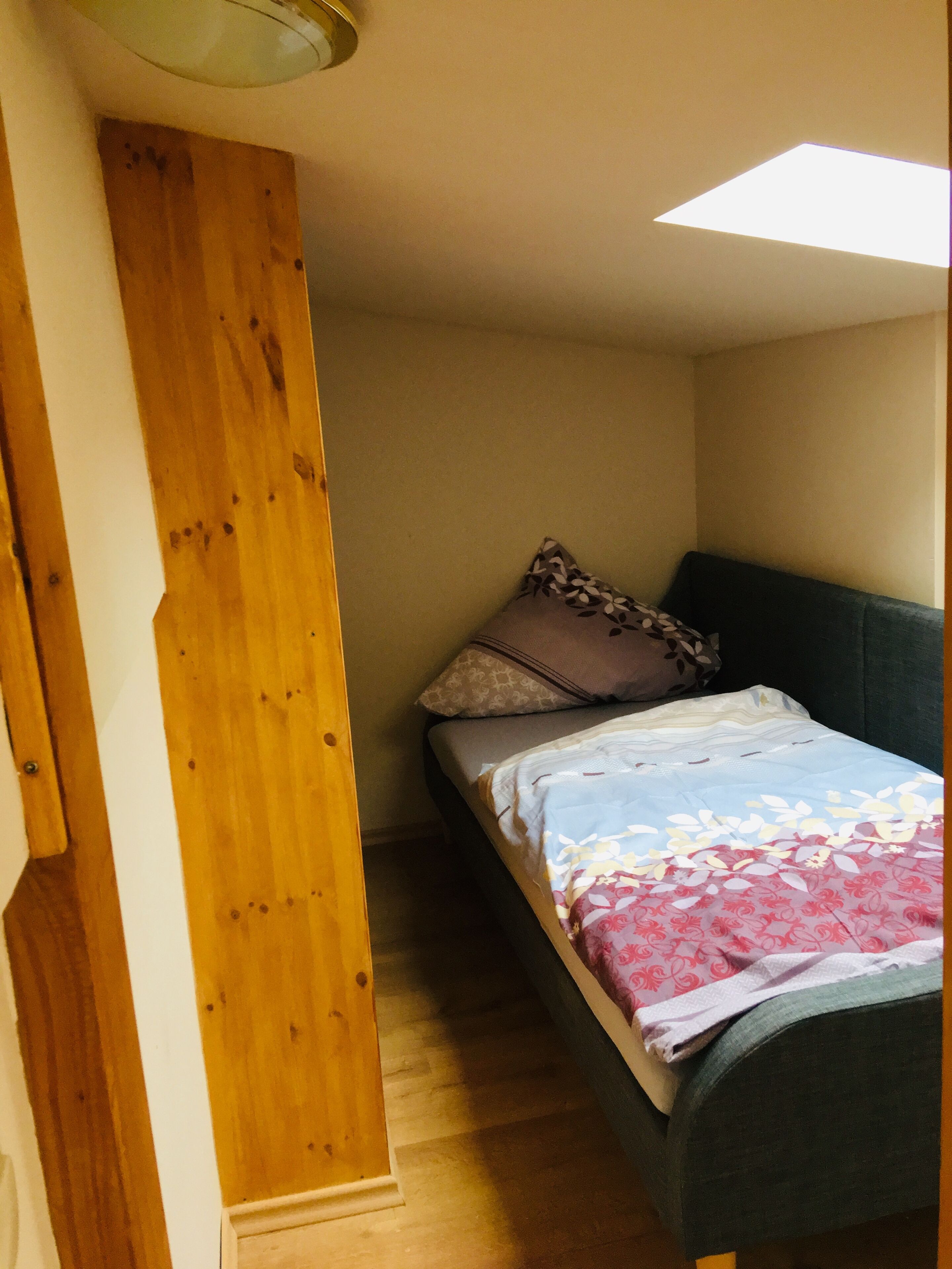 Una habitación pequeña y acogedora con una cama individual, pared de madera y techo inclinado.