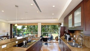 A modern kitchen with granite countertops, stainless steel appliances, and a dining area with a view of the outdoors. - Aloha Villas 3, Oceanfront Townhouse, Steps to The (Kihei)