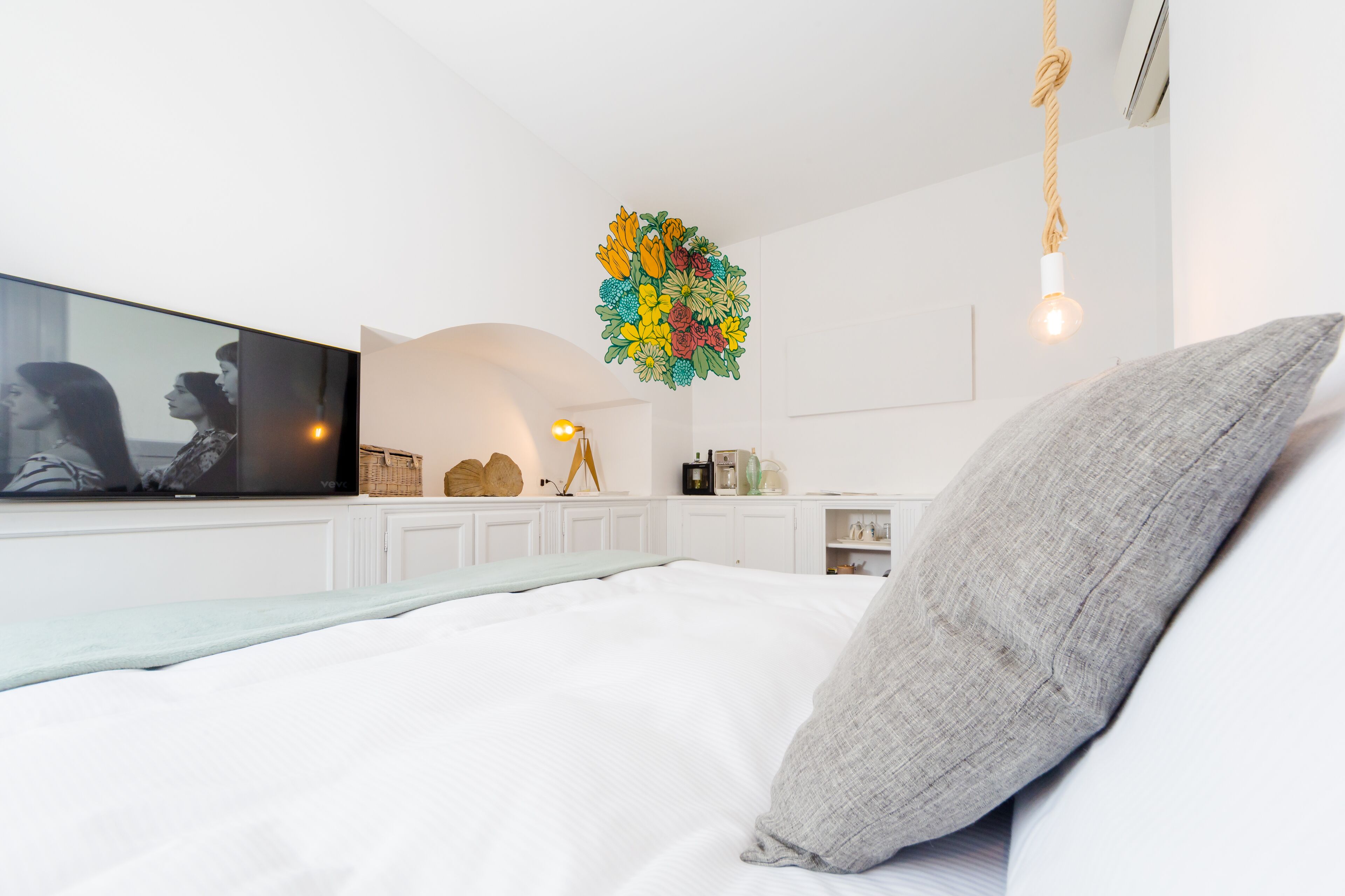 Ein modernes Schlafzimmer mit einem großen Bett, einem Flachbildfernseher, einem dekorativen Wandbild und einer Hängeleuchte.