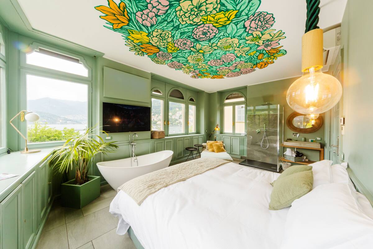 A bedroom with a large bed, a bathtub, and a view of the outdoors.