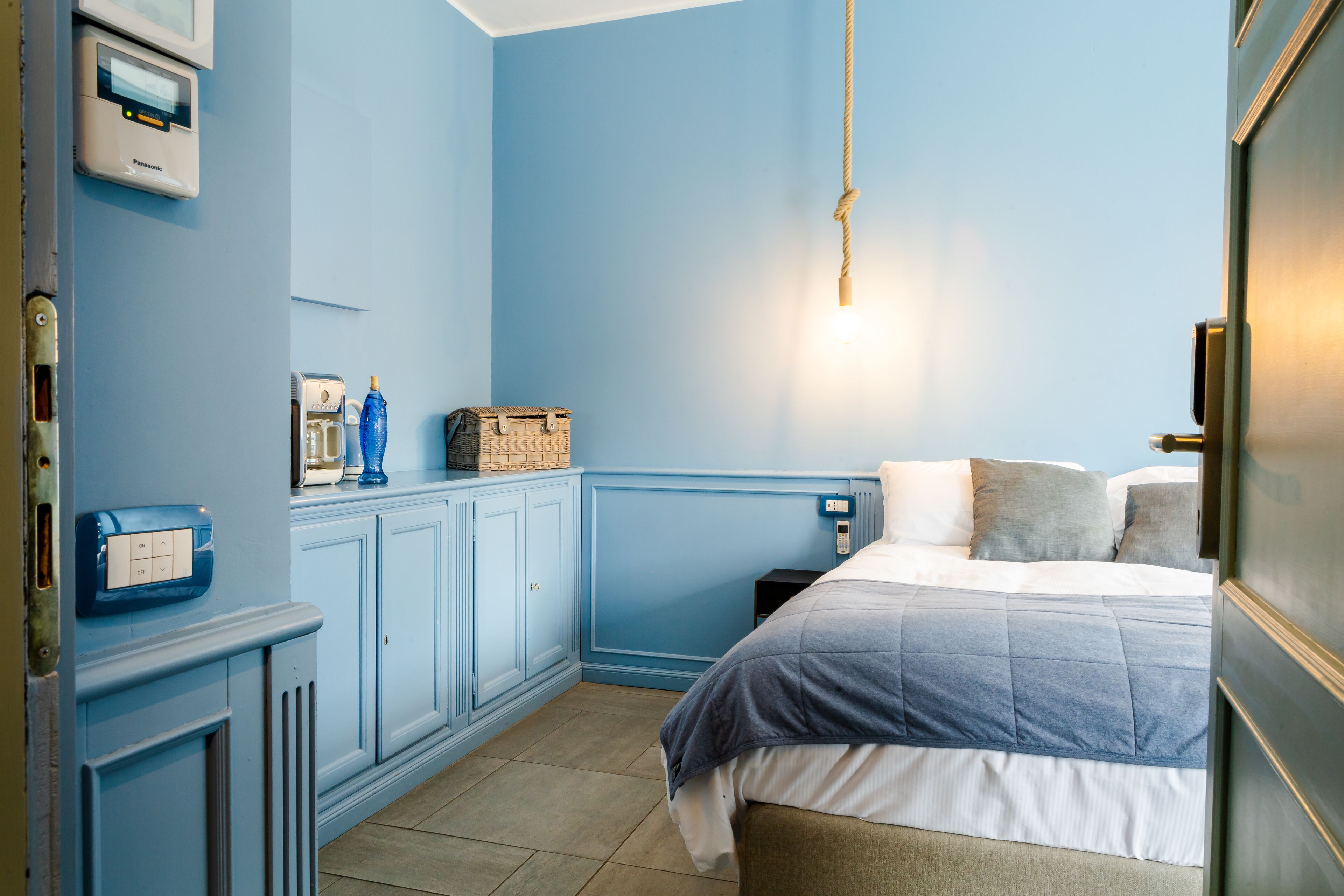 Een slaapkamer met een bed, nachtkastje, kledingkast, radiator en een aan de muur bevestigde thermostaat.