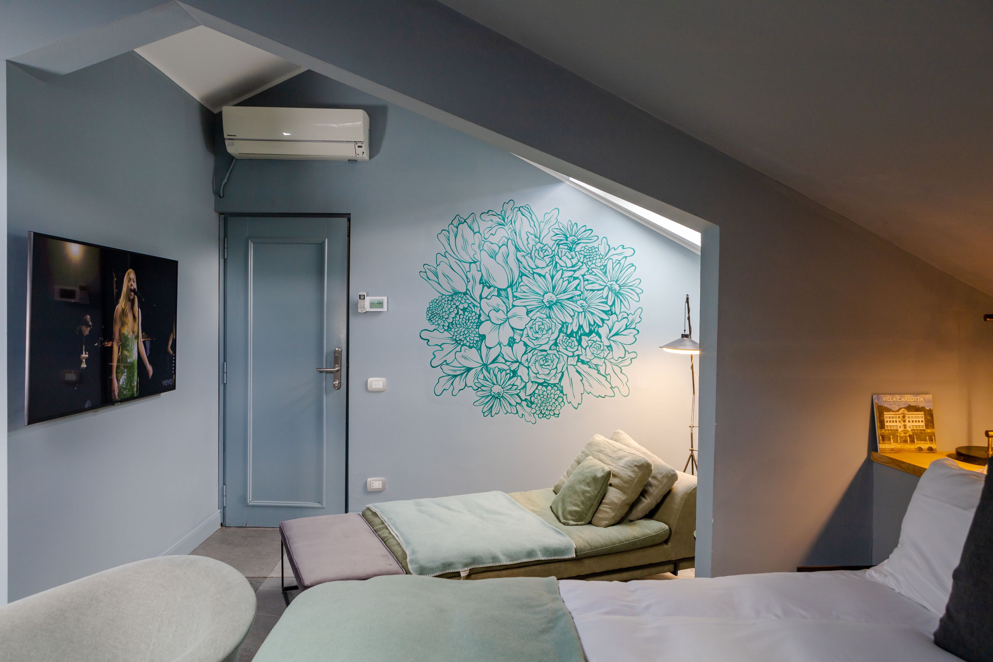 Ett hotellrum med en säng, en soffa, en vägg med ett blommönstrat dekorationsmotiv, en dörr och en luftkonditioneringsanläggning.