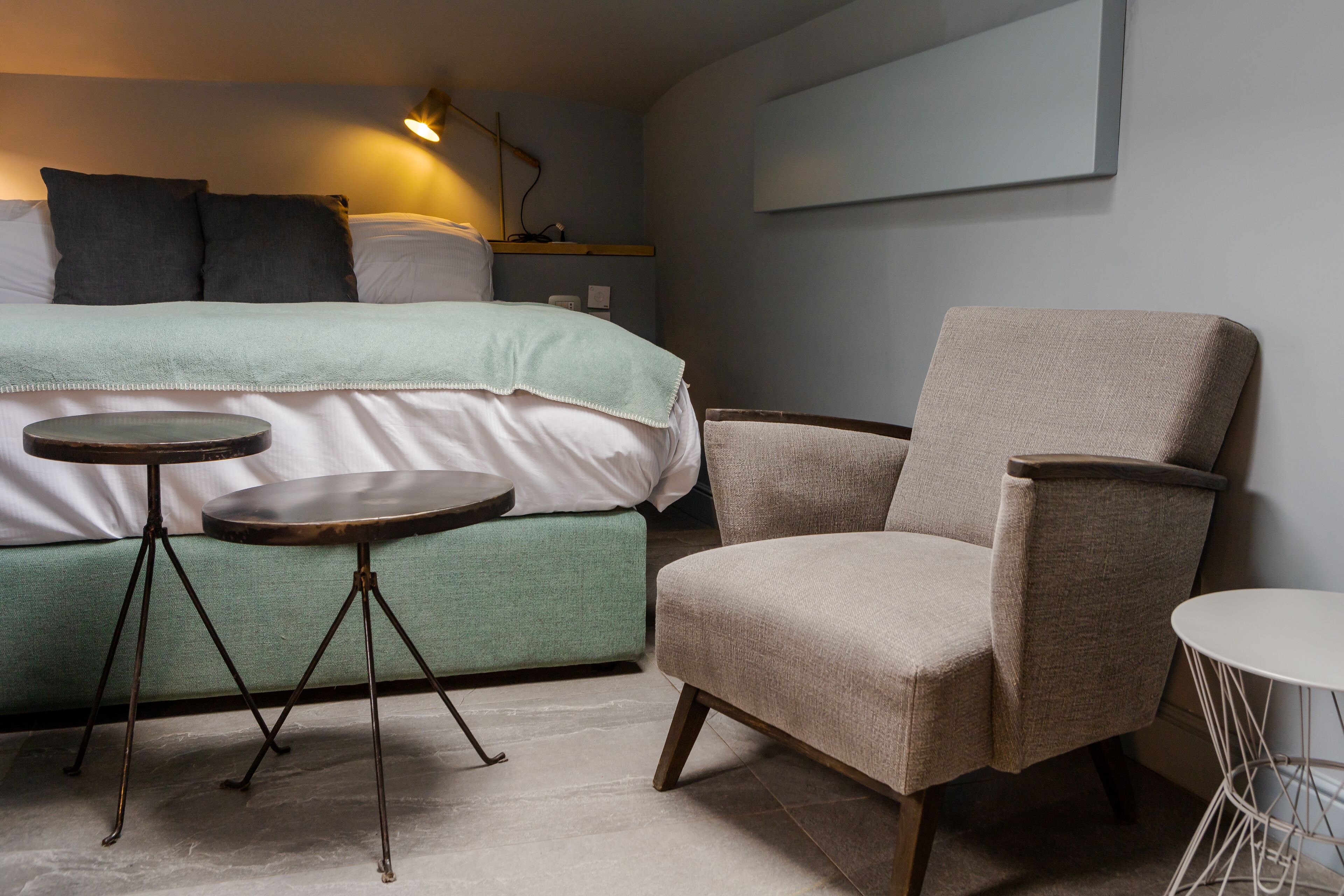 A bedroom with a bed, a chair, two small tables, and a wall-mounted TV.