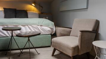 A bedroom with a bed, a chair, two small tables, and a wall-mounted TV.