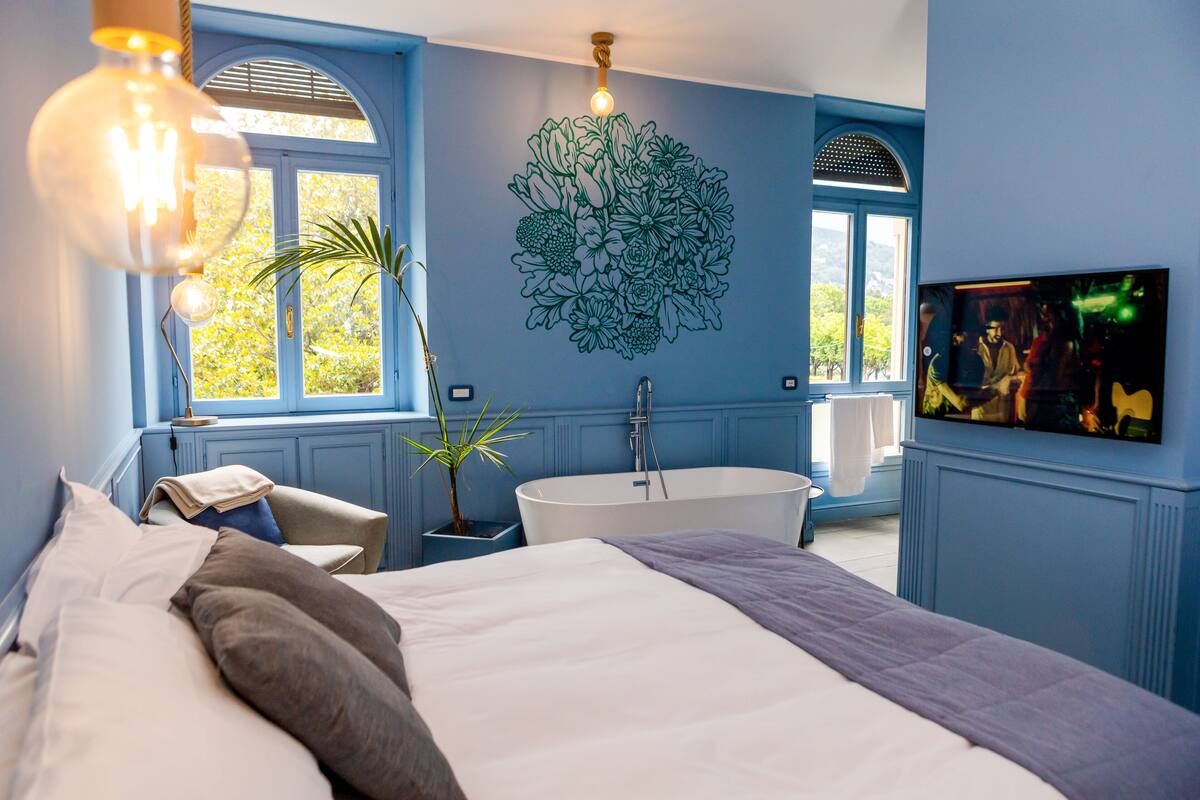A bedroom with a large bed, a bathtub, and a TV on the wall.