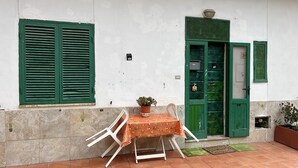 Een klein buiten zitgedeelte met een tafel, stoelen, een potplant en een groene deur.