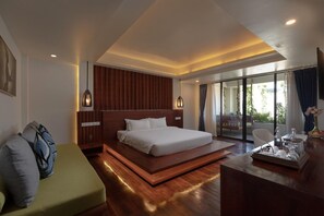 A modern hotel room with a large bed, a green sofa, a wooden desk, and a view of the outdoors through large windows. - Hari Residence & Spa (Siem Reap)