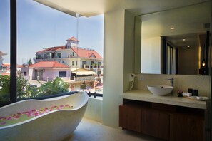 Une salle de bain moderne avec une baignoire sur pieds, un grand miroir et une vue sur un immeuble aux toits rouges.