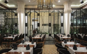 A restaurant with a modern interior, featuring a geometric patterned wall, wooden tables, and black chairs. - Hari Residence & Spa (Siem Reap)