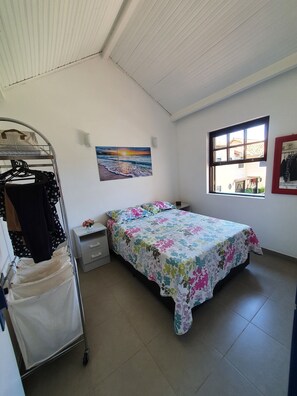 Un dormitorio con cama, un cuadro, una ventana y un perchero.