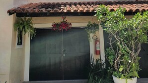 A building with a tiled roof, two windows with shutters, a closed garage door, and potted plants.
