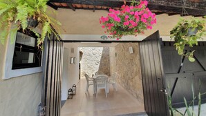 A covered outdoor area with a stone wall, a table with chairs, and hanging plants.