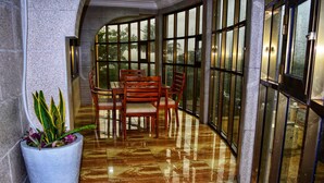 A corridor with a marble floor, a dining area with wooden furniture, and large windows with a view of greenery. - Regent Palace Hotel (Freetown)