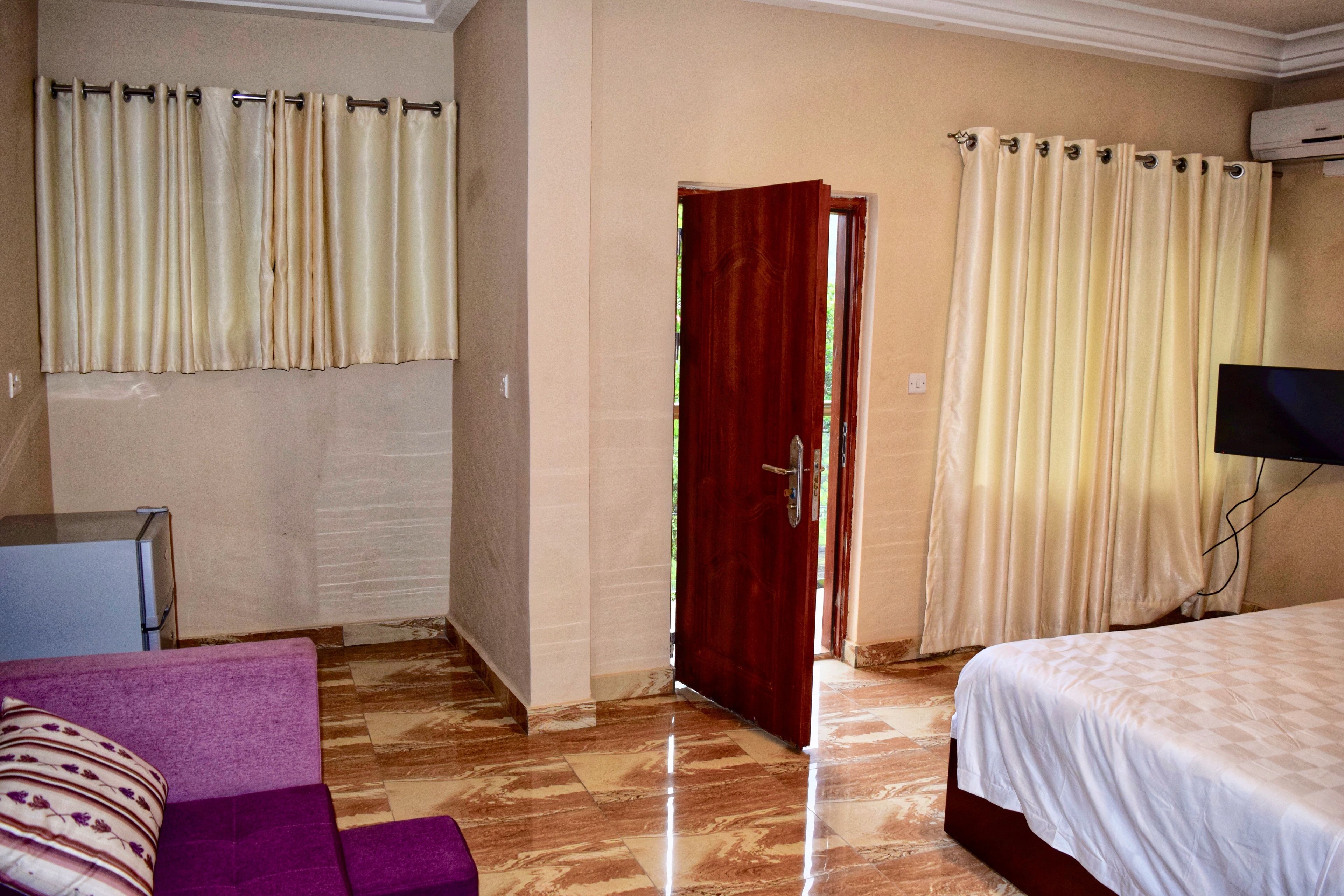 Una habitación de hotel con una cama, un sofá morado, una mesita pequeña y una puerta roja.