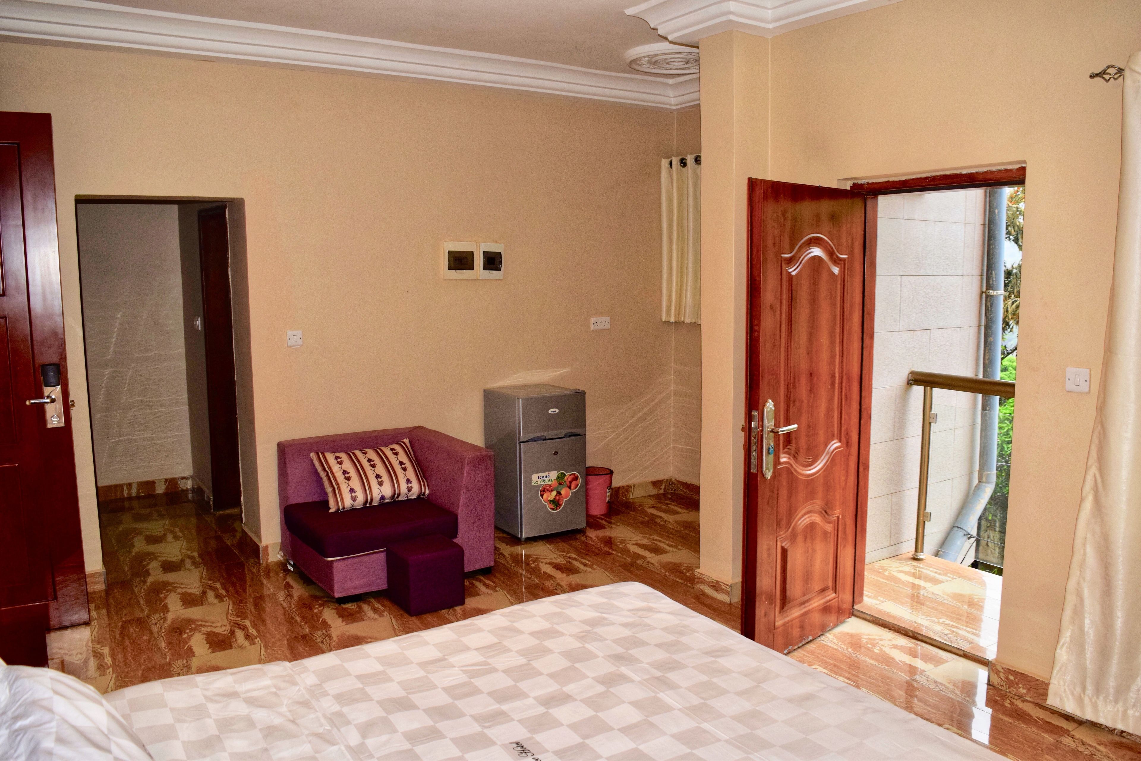 A hotel room with a bed, a small sofa, a refrigerator, and a door leading to a balcony.