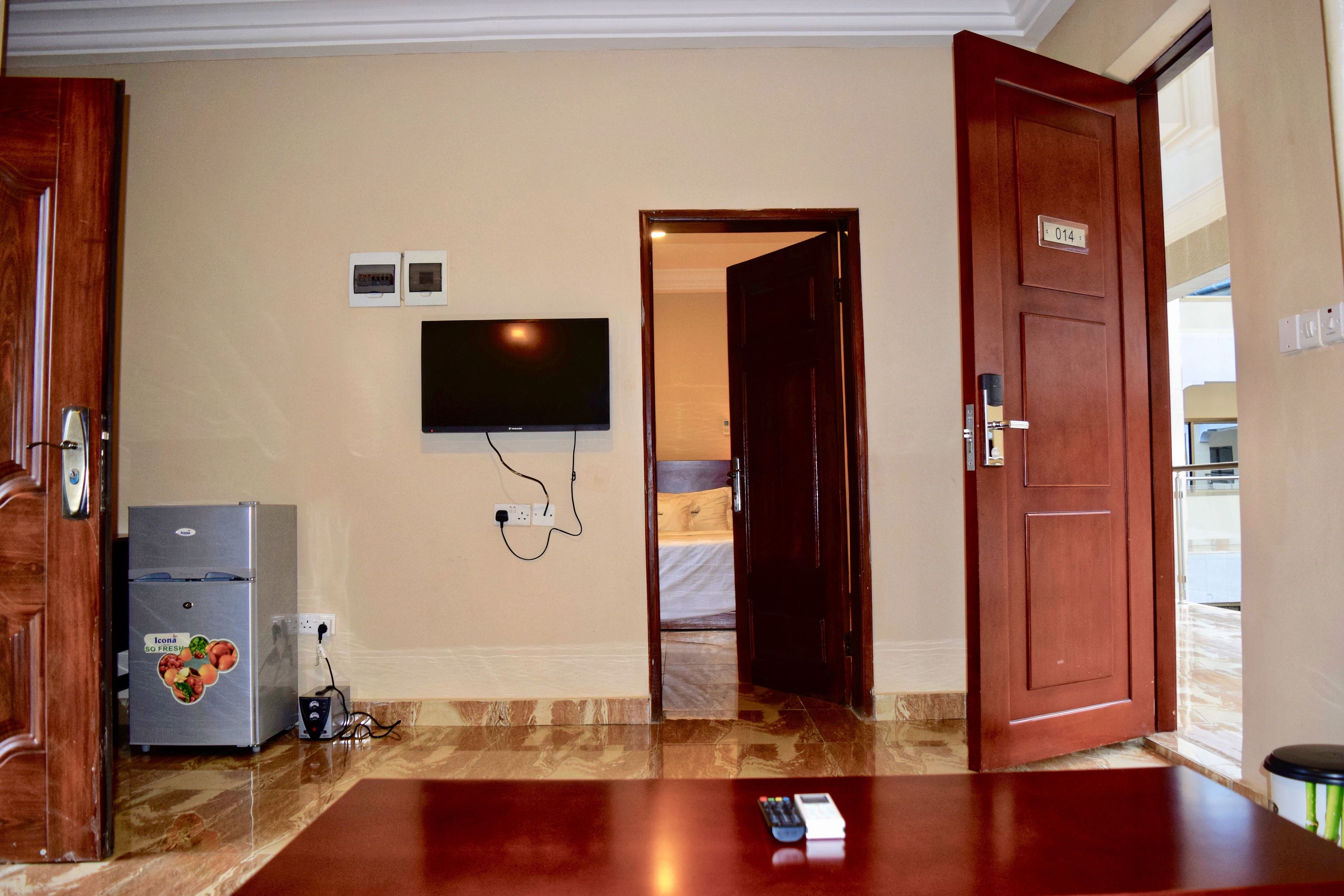 A hotel room with a flat-screen TV mounted on the wall, a refrigerator, a wooden door, and a sign with the number 014.