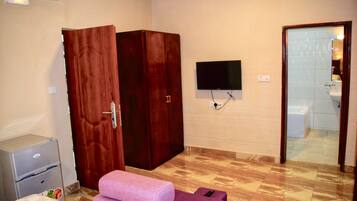 Ein Zimmer mit einem Bett, einem Kleiderschrank, einem Fernseher und einem durch eine geöffnete Tür einsehbaren Badezimmer.