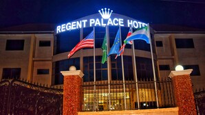 The exterior of Regent Palace Hotel with its name illuminated above the entrance, multiple flags, and a gated entrance. - Regent Palace Hotel (Freetown)