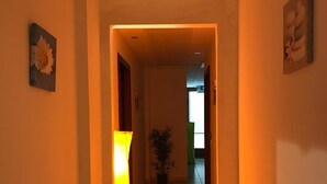 A hallway with a warm light source, a potted plant, and artwork on the walls. - Hotel Daisy (San Giovanni Lupatoto)