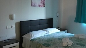 A neatly made bed with a quilt, a bedside table with a lamp, and a wall-mounted light fixture. - Hotel Daisy (San Giovanni Lupatoto)