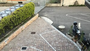A paved parking area with marked spaces, a gated entrance, and a scooter parked near the gate. - Hotel Daisy (San Giovanni Lupatoto)
