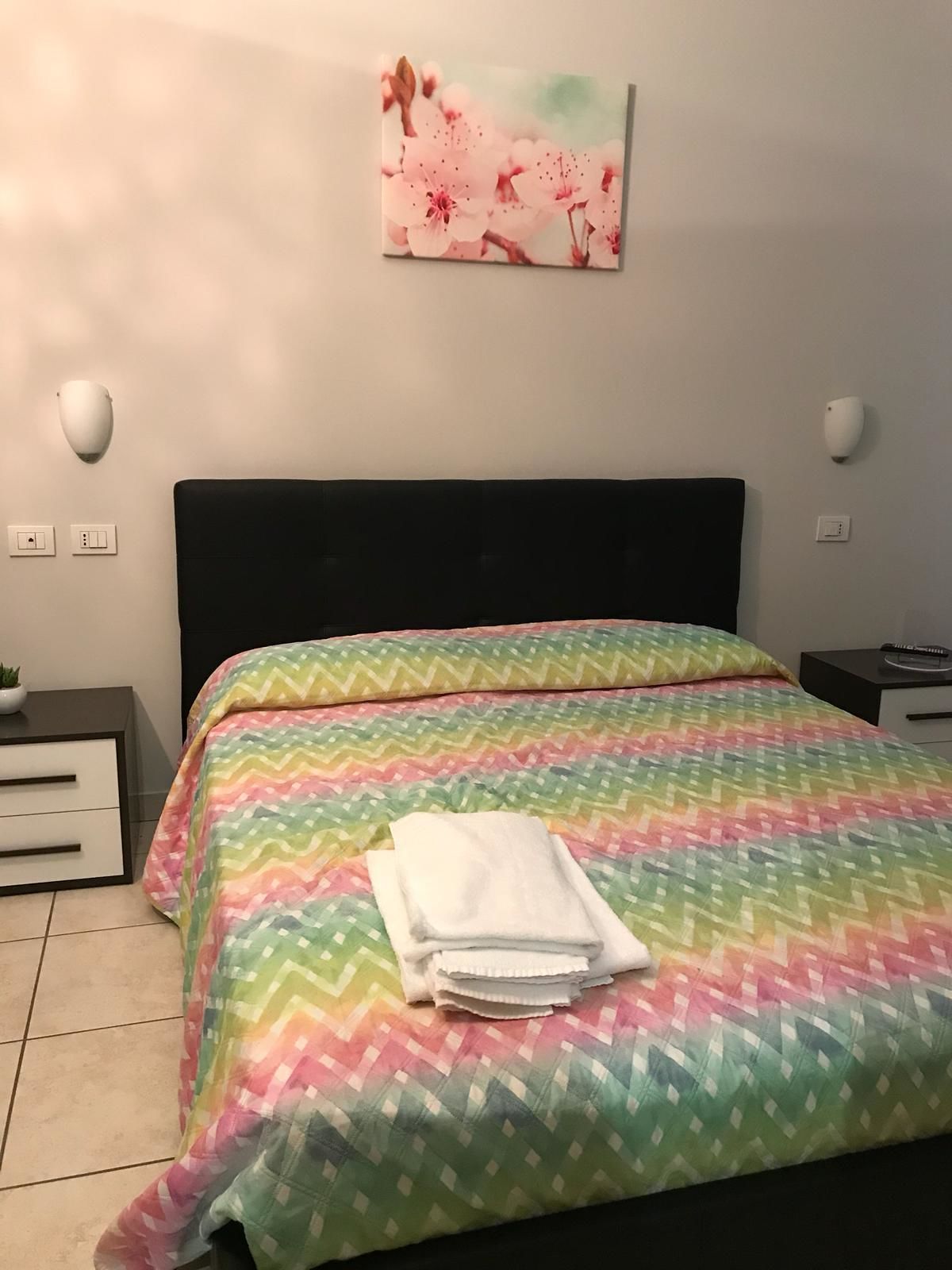 A neatly made bed with a colorful zigzag patterned bedspread and a stack of white towels.