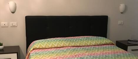 A neatly made bed with a colorful zigzag patterned bedspread and a stack of white towels.