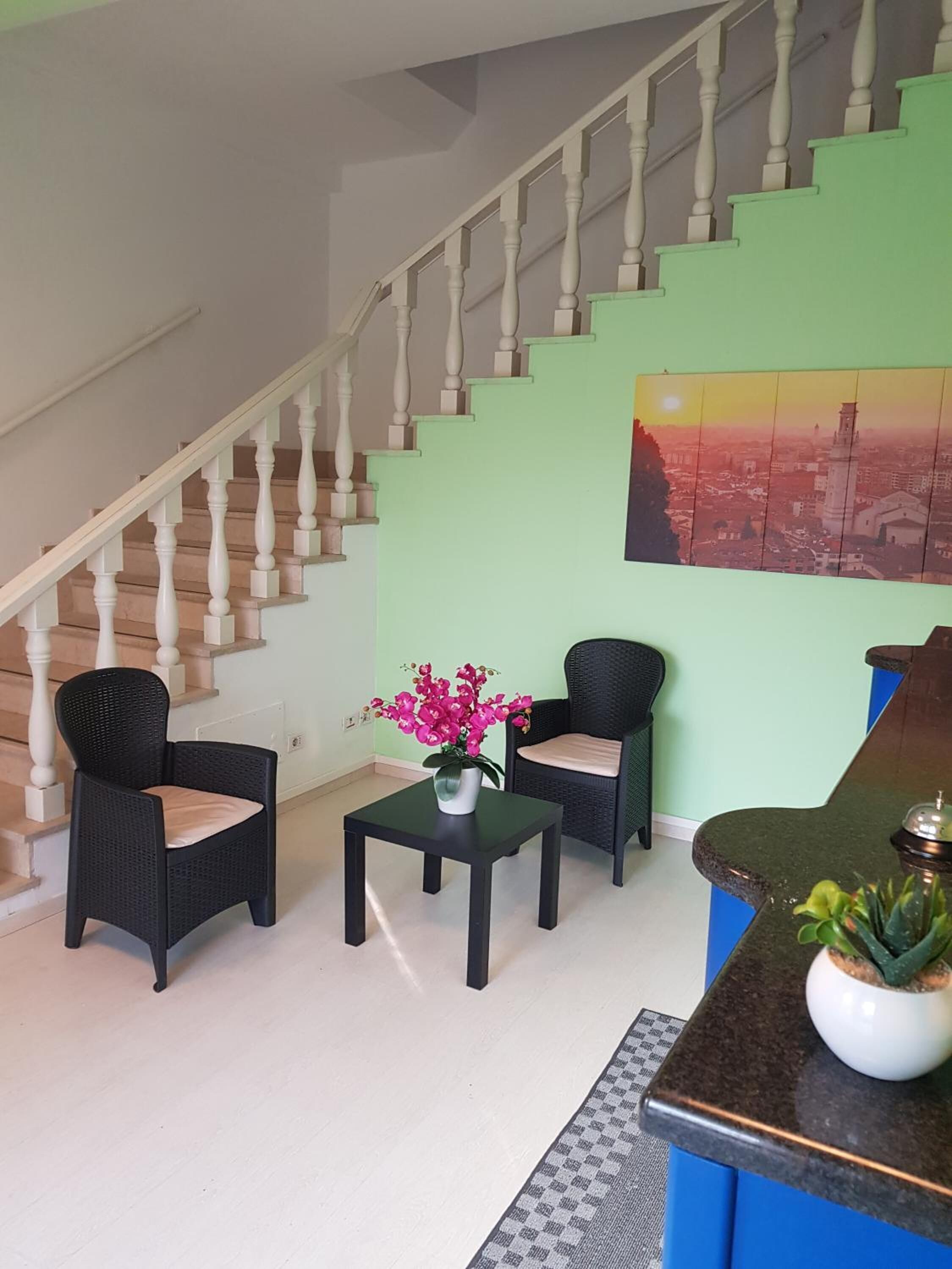 Eine Treppe mit weißen Balustraden führt zu einer Empore mit einer grünen Wand und einem Stadtbildgemälde.