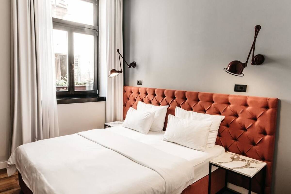 Una cama bien tendida con ropa de cama blanca, un cabecero naranja con botonadura y dos mesitas de noche con lámparas.