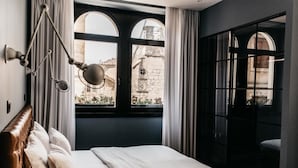 A bedroom with a large bed, a hanging lamp, and a view of a historic building through a window. - Abokamento Boutique Rooms (Split)