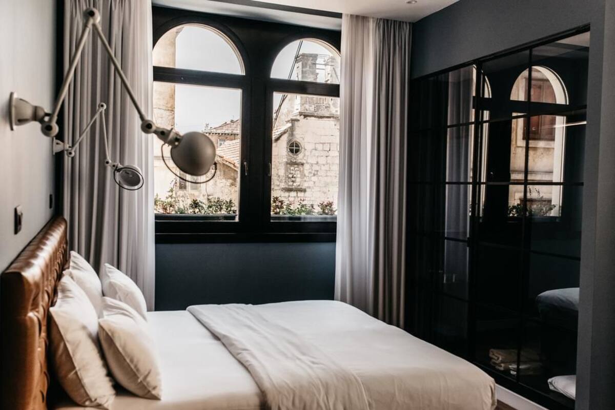 Un dormitorio con una cama grande, una lámpara colgante y vistas de un edificio histórico a través de una ventana.