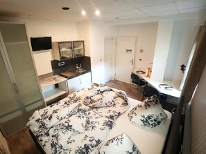 Una habitación compacta con cama, una kitchenette pequeña, un escritorio y una puerta.