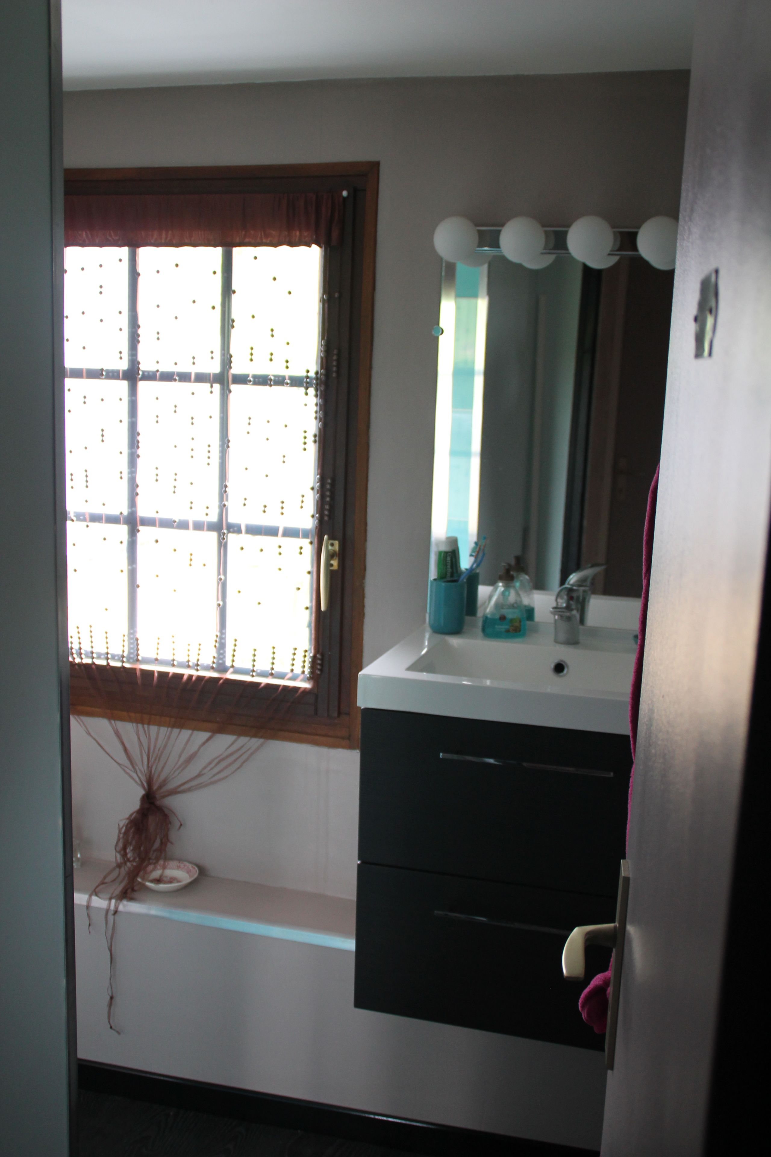 A bathroom with a window, sink, mirror, and towel rack.