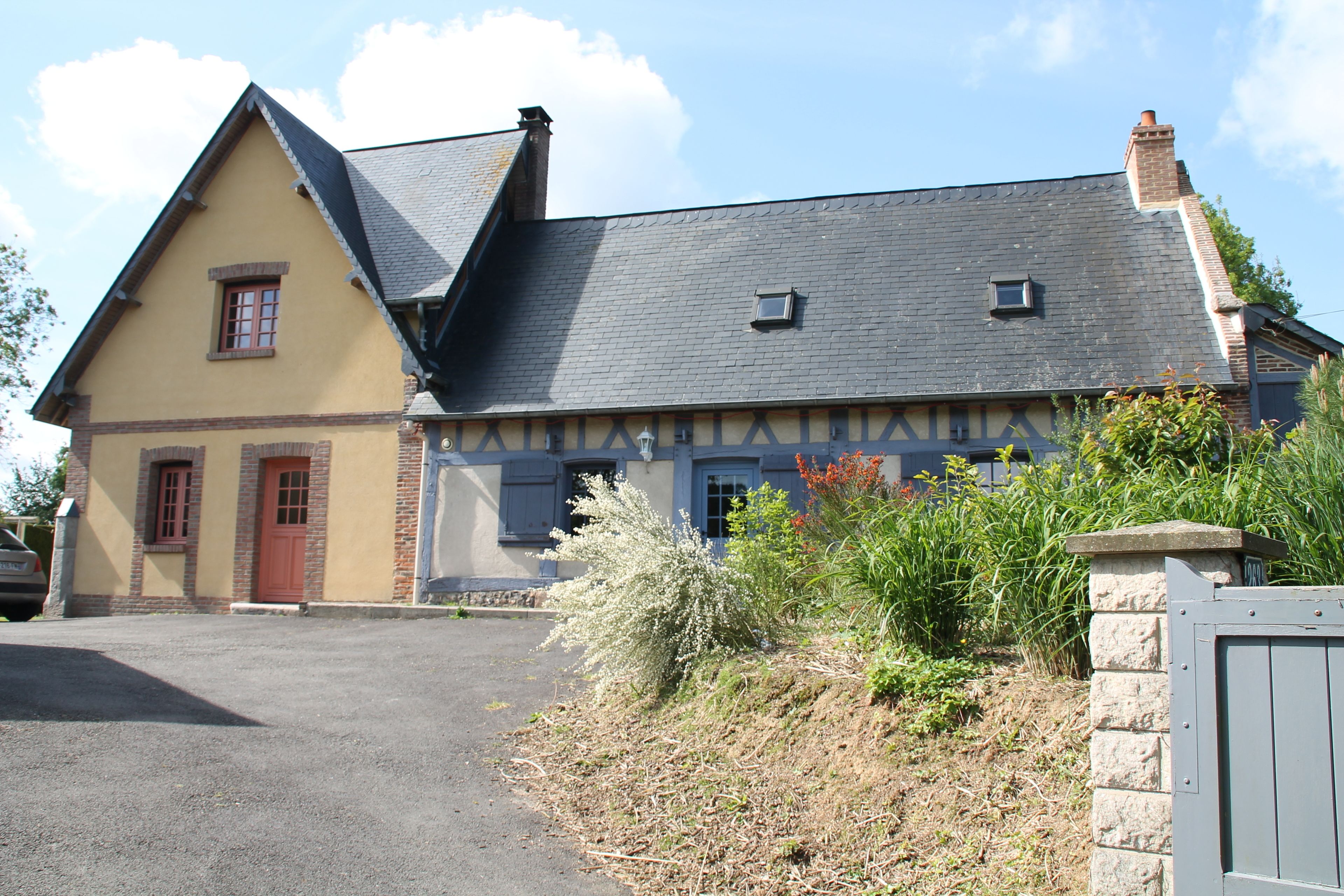 Une maison à deux étages, dotée d’un toit à forte pente, d’une cheminée bien visible et d’une petite fenêtre à l’étage supérieur.