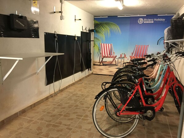 A bike rental station with multiple bicycles, a wall-mounted bike rack, and a beach-themed mural in the background.