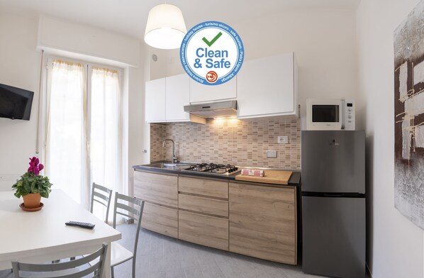 Una cocina moderna con estufa a gas, microondas y refrigerador. Hay una mesa de comedor con sillas y una planta en maceta.