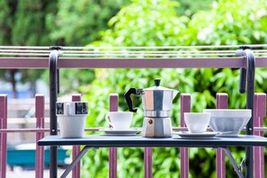 Una mesa con cafetera, tazas y platos, colocada al aire libre sobre un fondo verde.