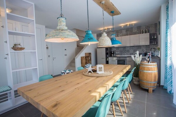 Une cuisine moderne avec des meubles blancs, une table à manger en bois, des chaises de couleur turquoise et des luminaires suspendus.