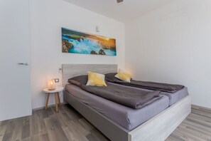 Une chambre à coucher comprenant un lit, une table de chevet, un tableau accroché au mur et une petite table avec une lampe.